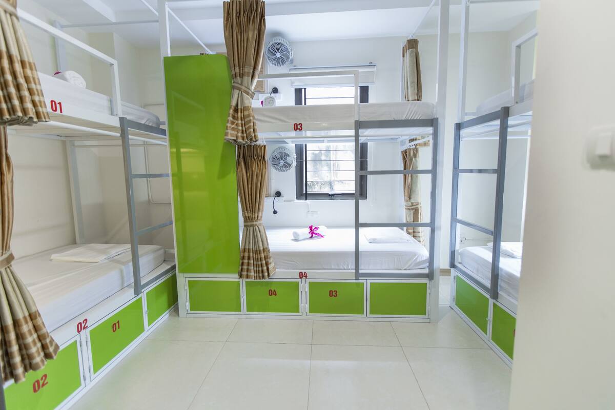 A dormitory room with bunk beds, numbered compartments, and a window with curtains.