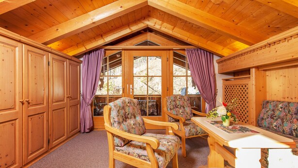 A wooden interior with a high ceiling, a dining table with chairs, and a sofa. - Haus Hubertus (Reit im Winkl)