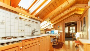 A wooden kitchen with a tiled backsplash, a microwave, and a dining area with a table and chairs. - Haus Hubertus (Reit im Winkl)