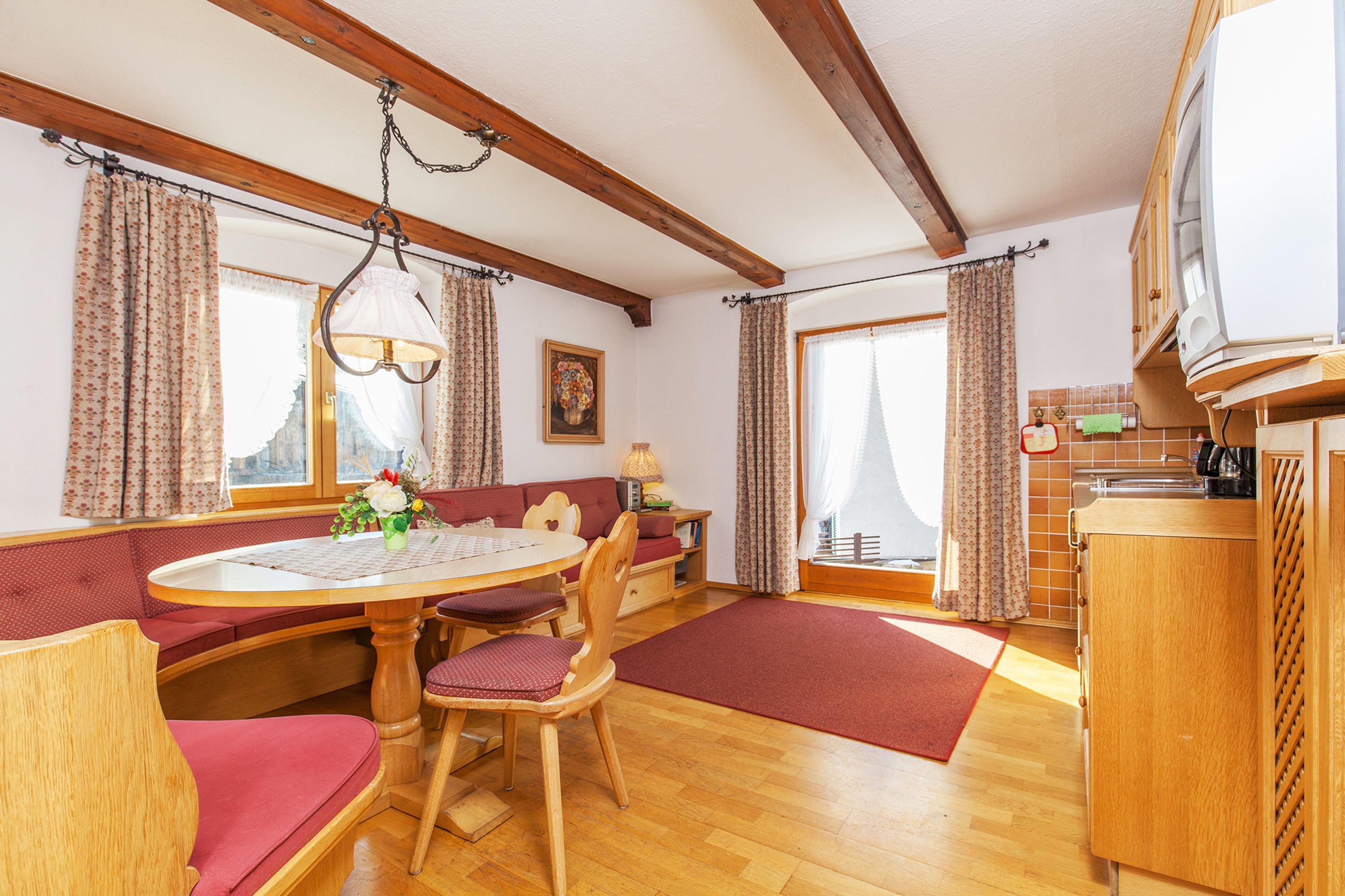 A cozy room with a wooden dining table, red cushioned seating, a wooden cabinet, and a television.
