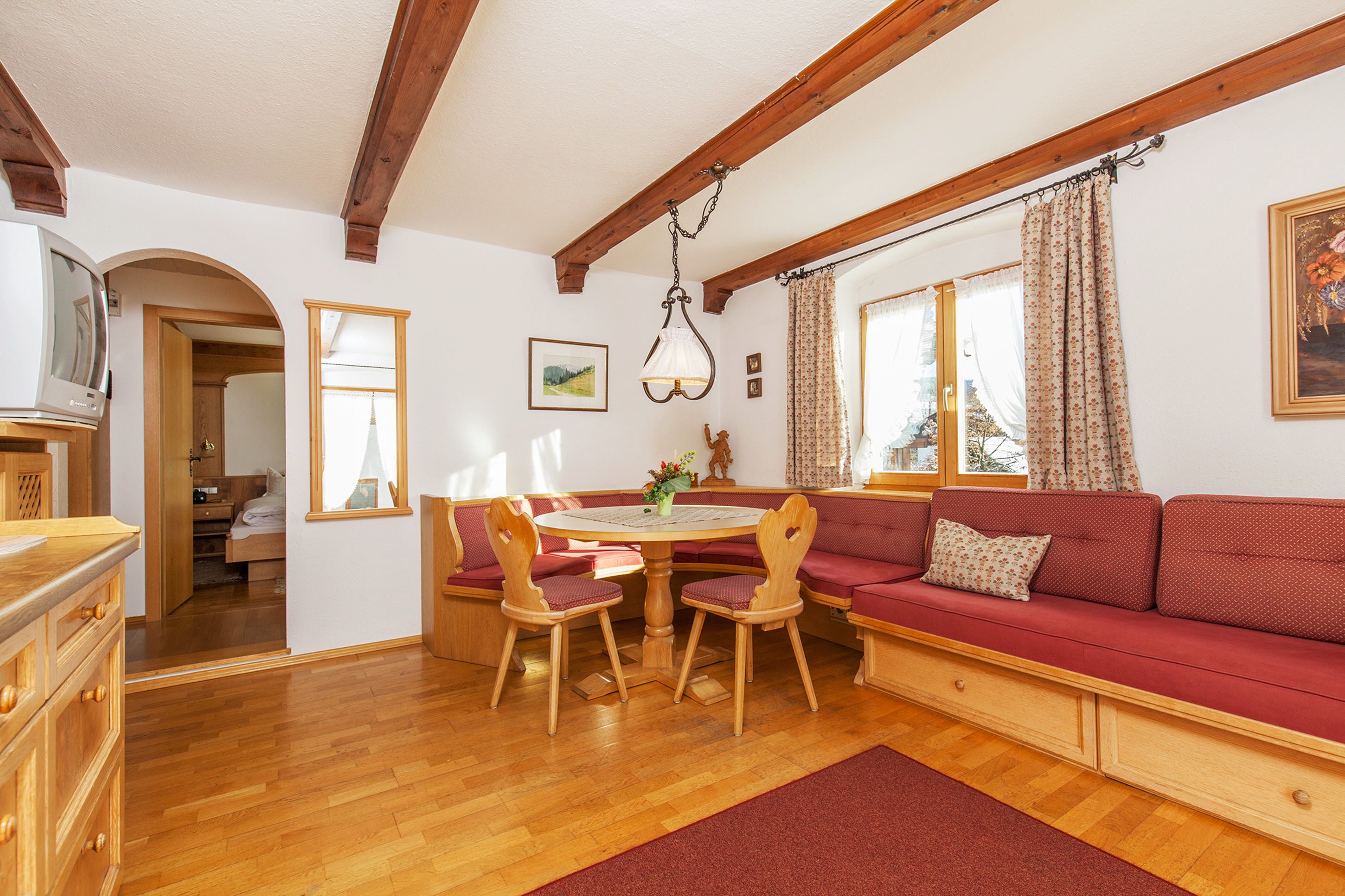 Une pièce chaleureuse avec une table à manger en bois, un canapé rouge et des chaises en bois. On y trouve également un buffet en bois et un miroir accroché au mur.