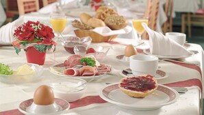 A breakfast setting with various food items, including bread, eggs, and pastries, arranged on a table with a white tablecloth.