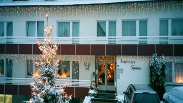 A hotel with a snow-covered entrance, a Christmas tree, and a sign that reads "Gasthof Specker."