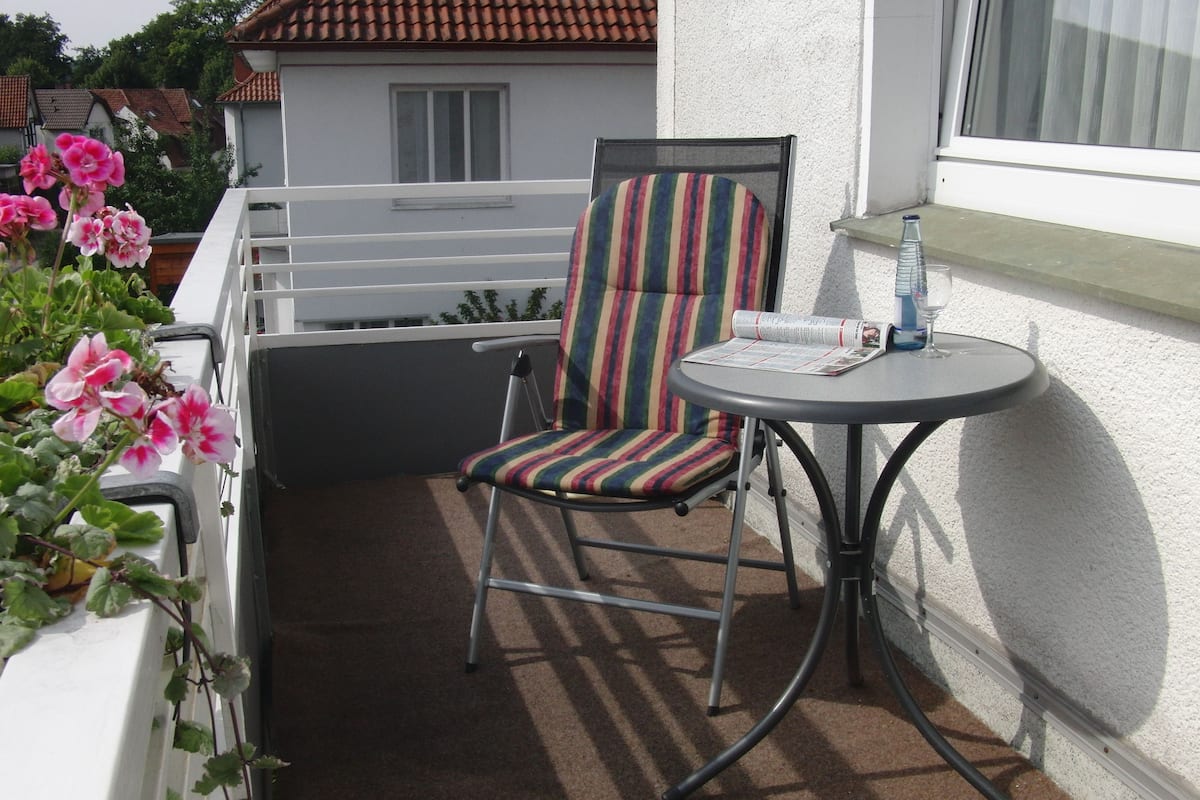 Un balcon avec une chaise et une petite table, une balustrade blanche et une fenêtre avec un rideau.