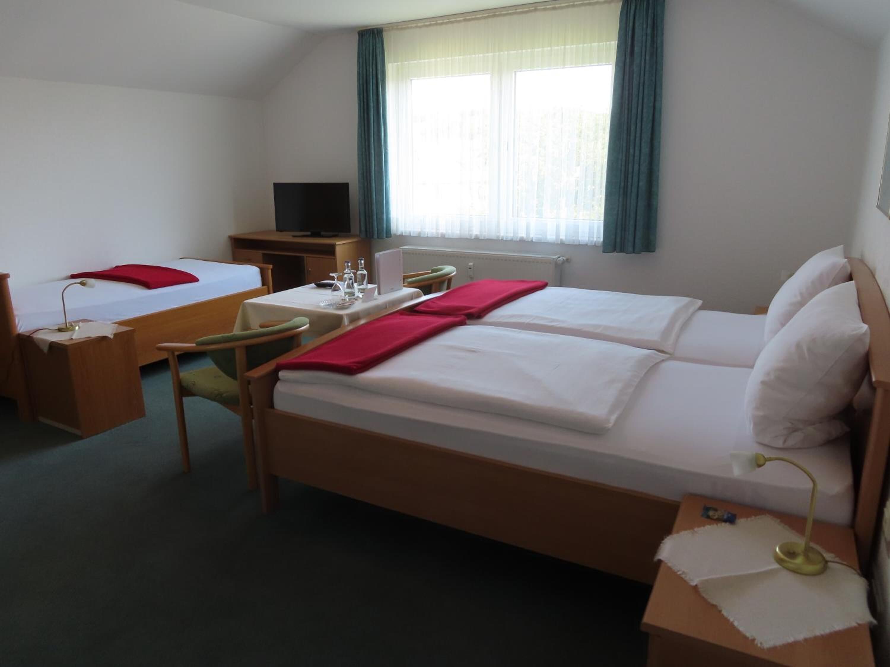 A hotel room with two single beds, a desk with a computer, a TV, and a window with curtains.