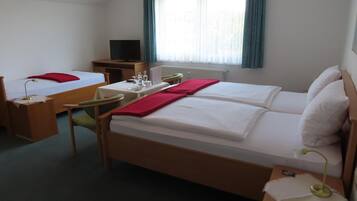 A hotel room with two single beds, a desk with a computer, a TV, and a window with curtains.