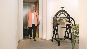 A person exiting an elevator into a hallway with a vintage-style table with a plant.