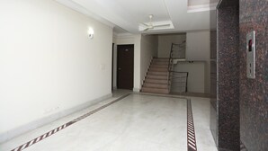 A spacious hallway with a marble floor, a staircase, and a ceiling fan. - OYO 15822 Ryan Residency (Gurugram)