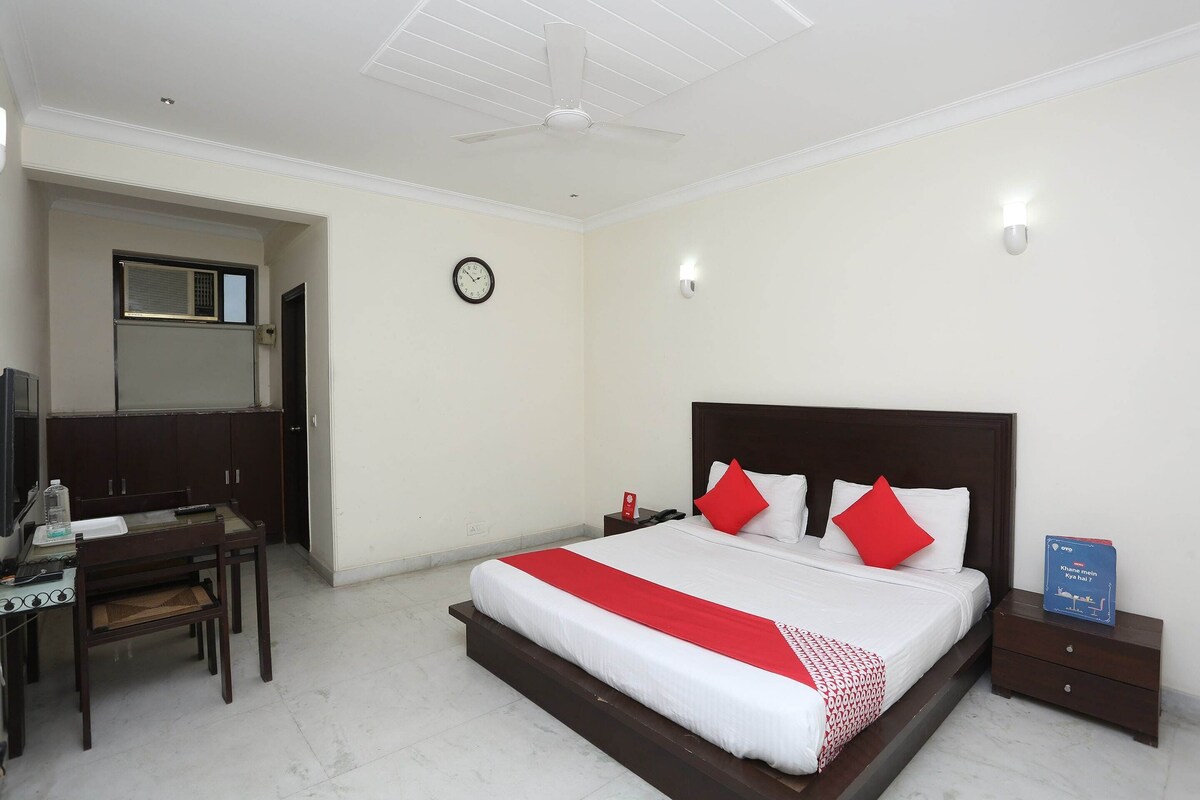 A hotel room with a bed, bedside tables, a desk, a chair, a clock, and a ceiling fan.
