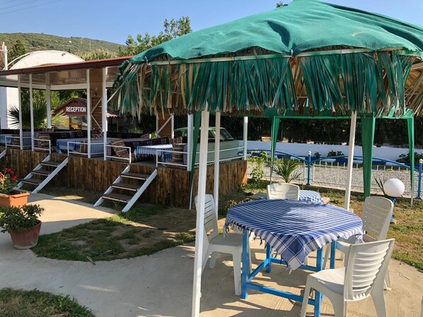 A covered outdoor seating area with a reception desk, a staircase, and a table with chairs. - New Iday Hotel (Kusadasi)