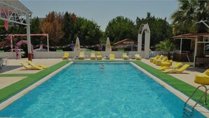 A rectangular swimming pool with a clear blue water, surrounded by yellow lounge chairs and a reception area in the background. - New Iday Hotel (Kusadasi)