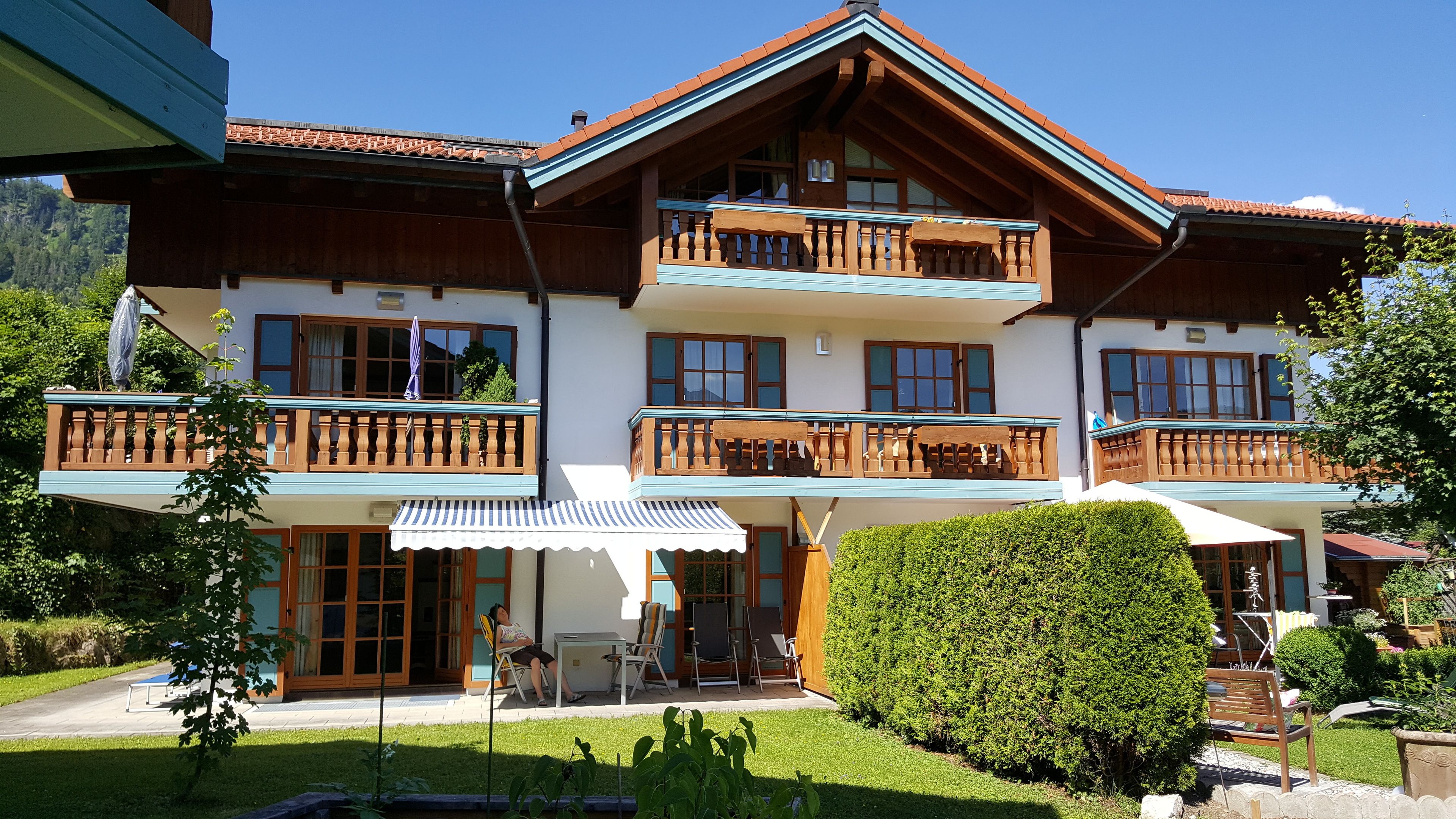 A two-story chalet with wooden balconies, a covered patio, and a well-maintained garden.