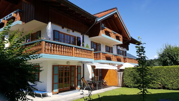 A two-story house with a balcony, a covered patio, and a well-maintained lawn. - Evis Wohnung (Reit im Winkl)