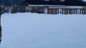 A cabin with a snow-covered roof, surrounded by a wooden fence and a snow-covered ground. - Evis Wohnung (Reit im Winkl)
