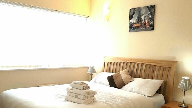 A neatly made bed with a headboard, a bedside lamp, and a folded towel on the bed. - Sub Penthouse Canary Wharf London (London)