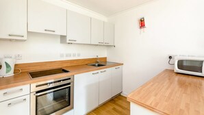 A compact kitchen with white cabinets, a wooden countertop, a built-in oven, a microwave, and a sink. - Sub Penthouse Canary Wharf London (London)