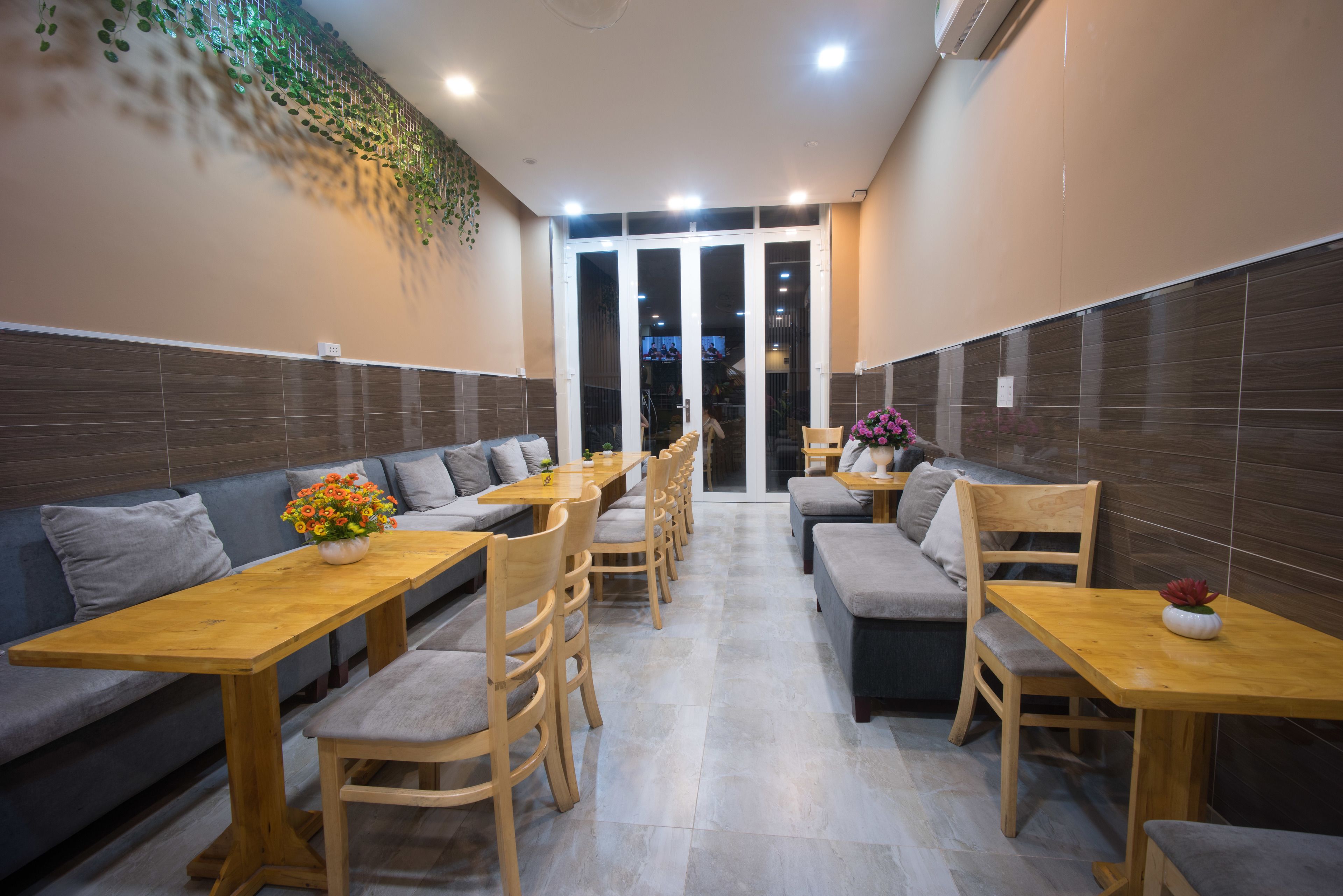 A modern dining area with wooden tables and benches, a large window, and a decorative plant wall.