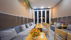 A modern dining area with a long wooden table, grey sofas, and wooden chairs. - Language Exchange Hostel 1 (Ho Chi Minh City)