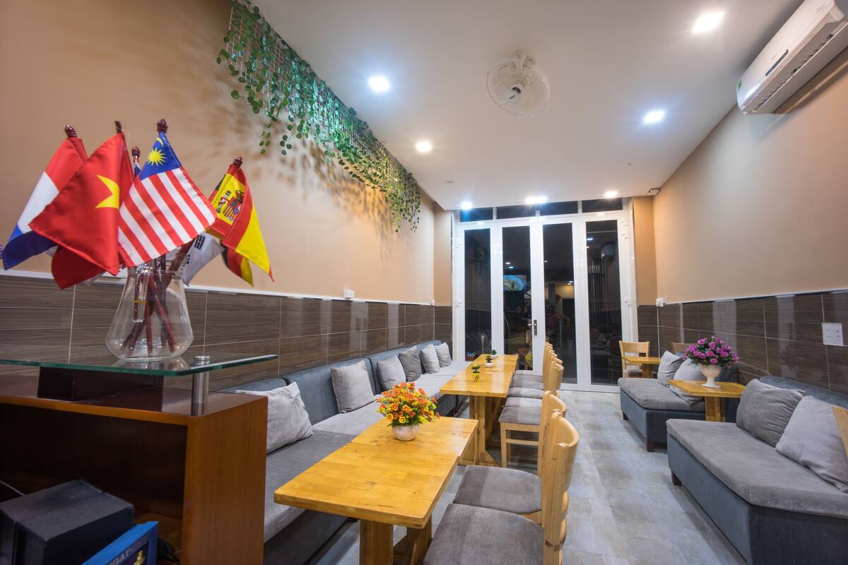 Um restaurante com um balcão comprido, diversas opções de assento incluindo cabines e mesas, e uma parede decorativa com bandeiras.