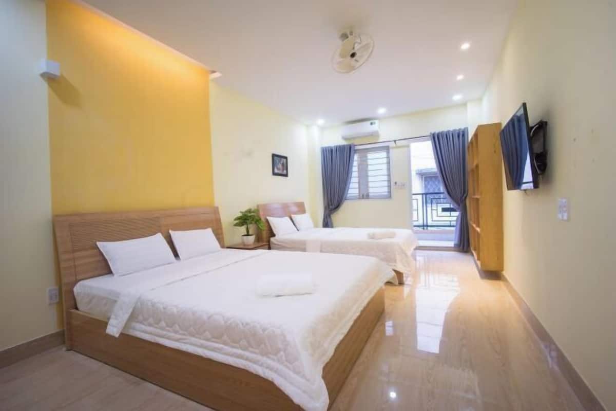 Quarto de hotel com duas camas, televisão, janela com cortinas e varanda.