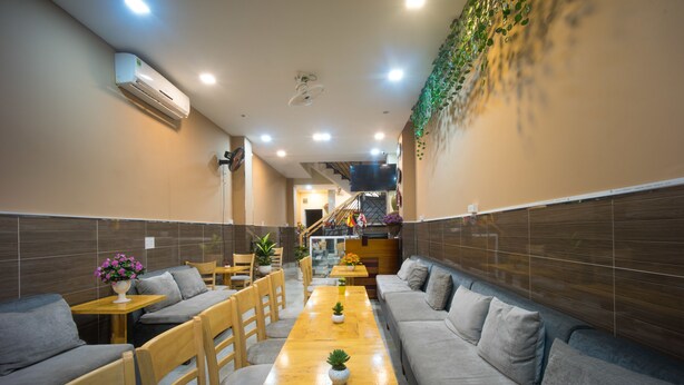 A modern interior with grey sofas, wooden tables, and a long wooden bench. - Language Exchange Hostel 1 (Ho Chi Minh City)