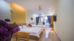 A hotel room with two beds, a wooden chair, a small table, a potted plant, and a TV mounted on the wall. - Language Exchange Hostel 1 (Ho Chi Minh City)