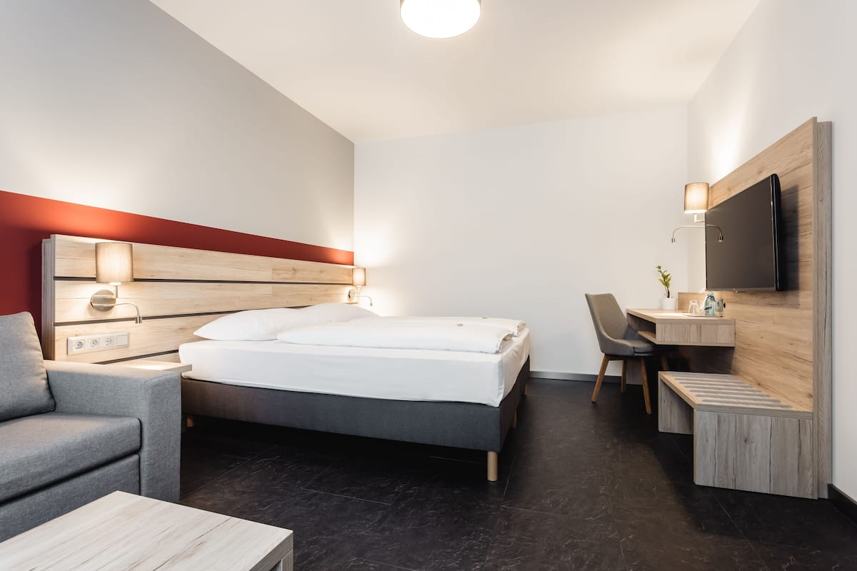 A modern hotel room with a bed, a desk, a chair, and a TV mounted on the wall.
