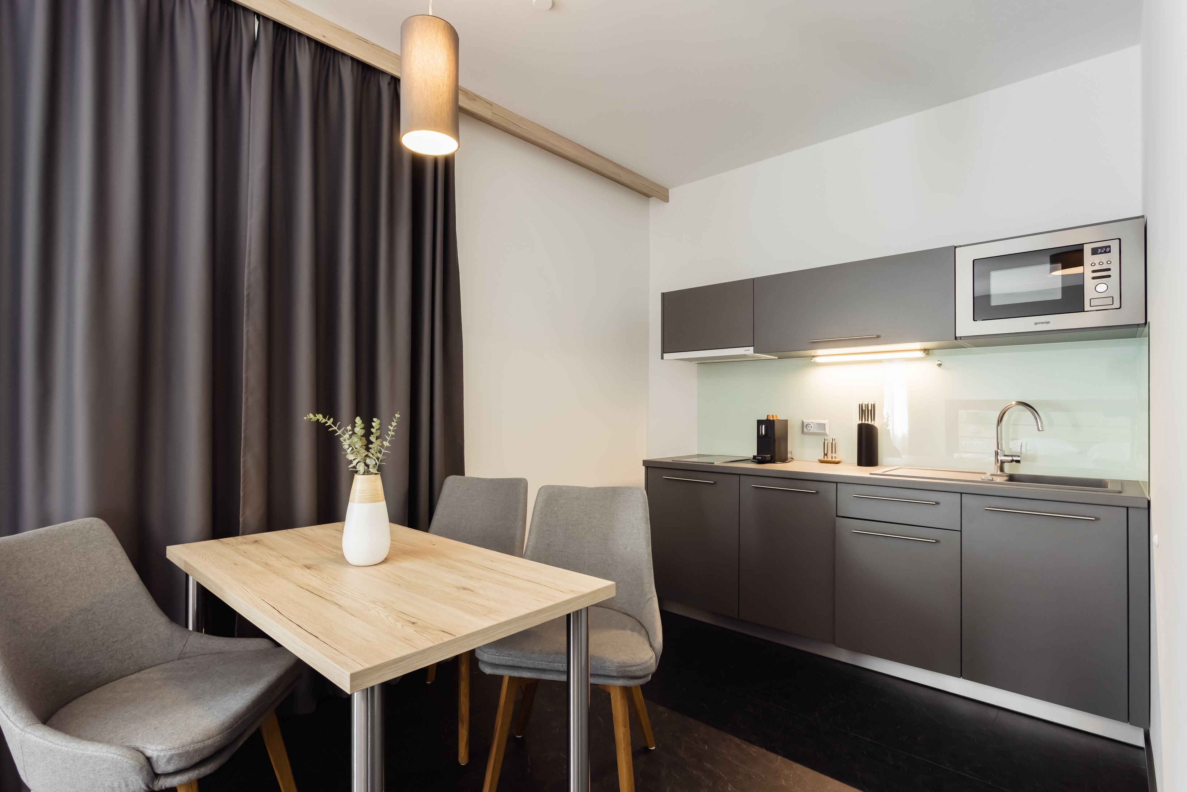 A modern kitchen with a microwave, sink, and cabinets. There is a dining table with chairs and a vase with flowers.