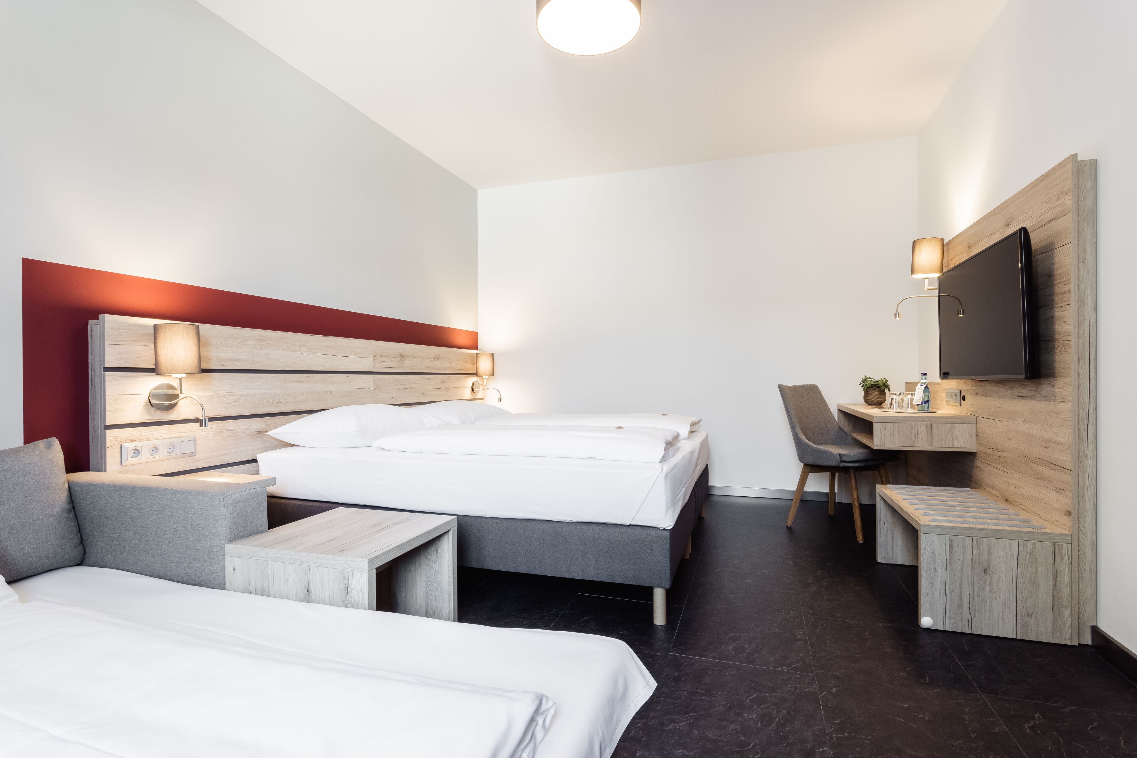 A modern hotel room with two beds, a desk, a chair, and a TV mounted on the wall.