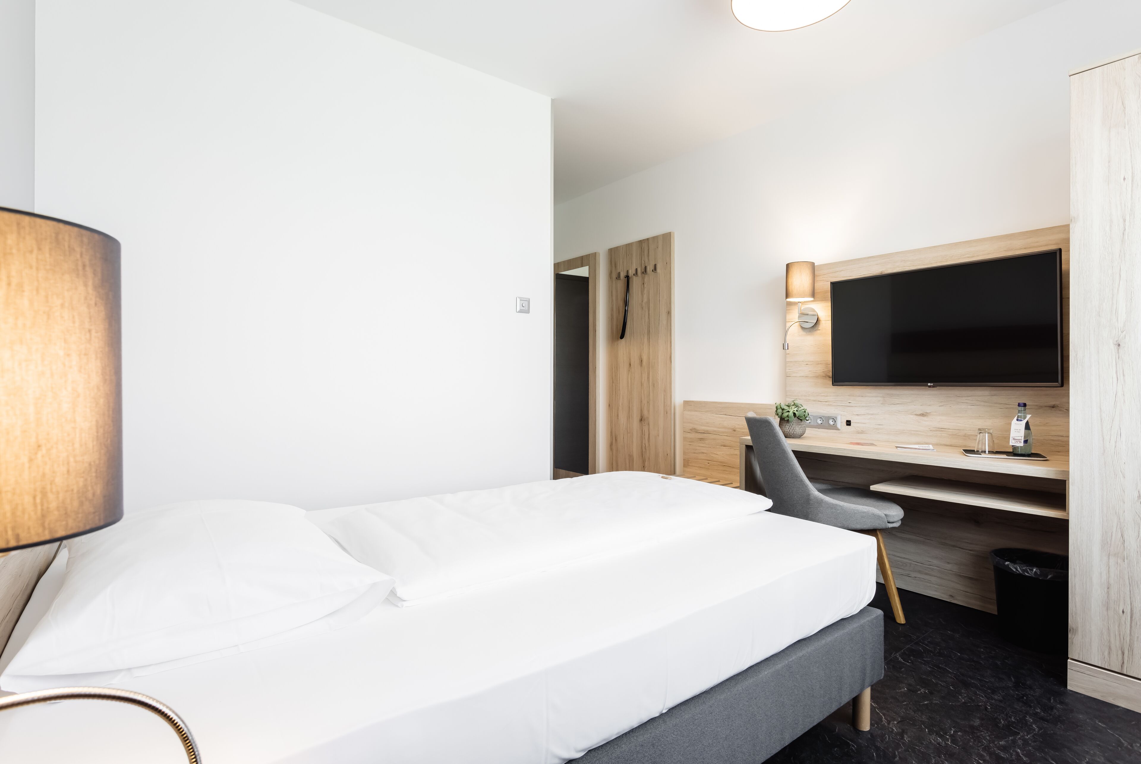 Una habitación de hotel con una cama, un escritorio, una silla, un televisor y un armario.
