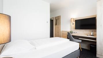 Una habitación de hotel con una cama, un escritorio, una silla, un televisor y un armario.