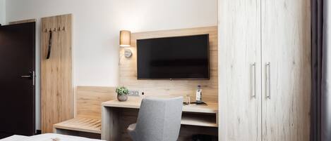 A hotel room with a bed, a desk with a chair, a TV, and a wardrobe.