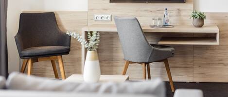 Una sala moderna con un sofá, dos sillones, una mesita de centro, un televisor montado en la pared y una pequeña planta en la mesita auxiliar.