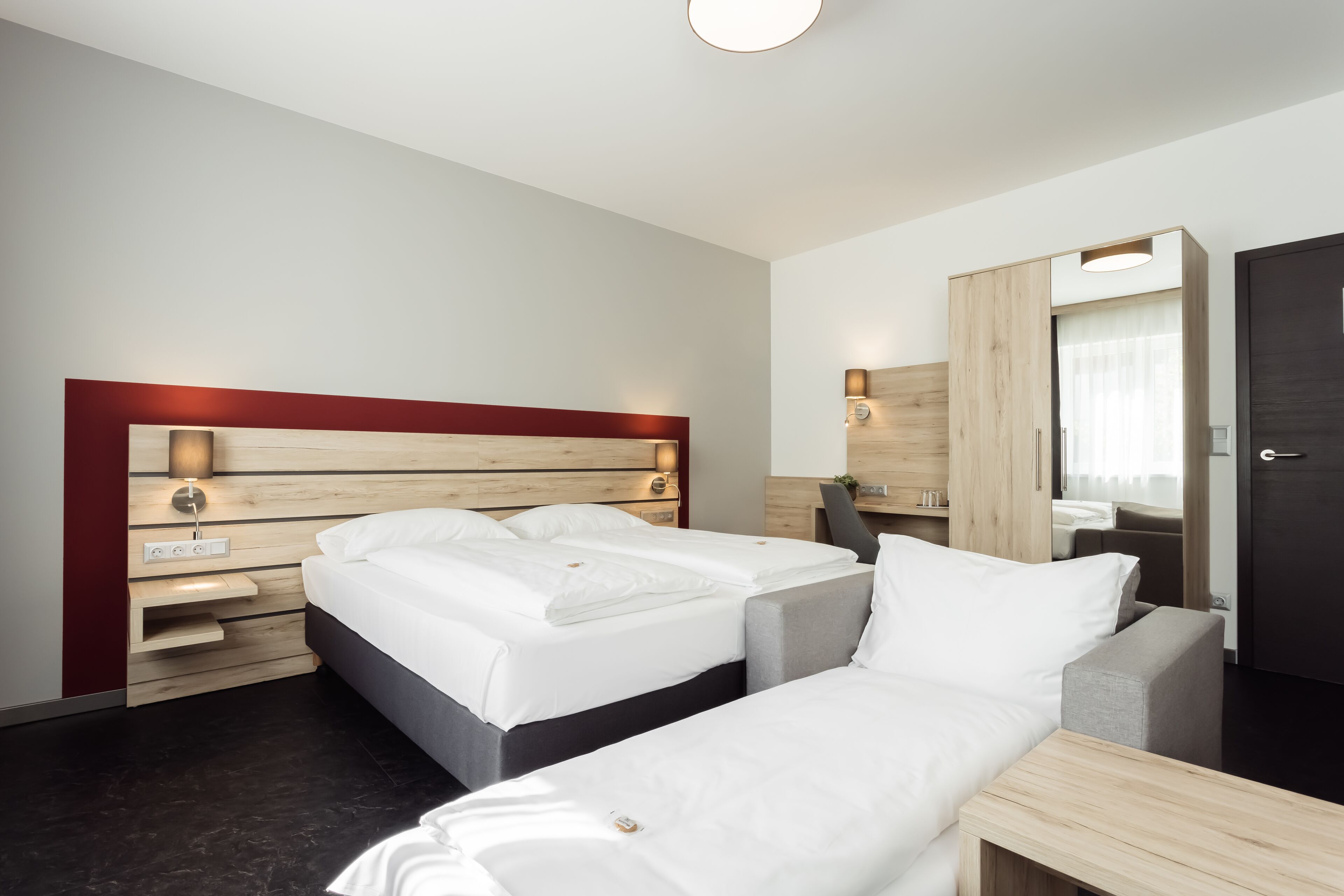 A hotel room with two beds, a wooden headboard, a bedside table, a mirror, and a wardrobe.