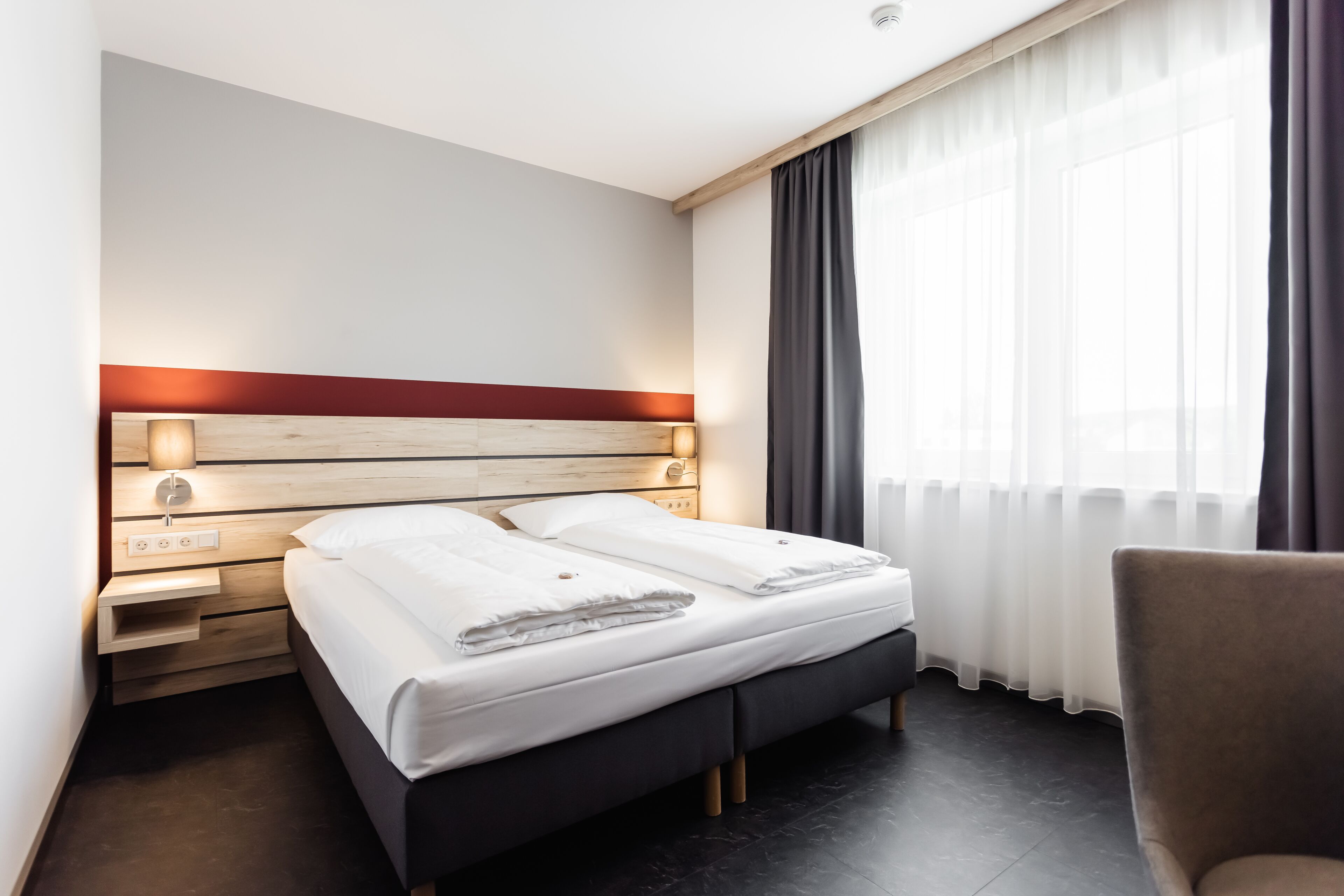 A hotel room with a bed, bedside table, lamp, and a chair.