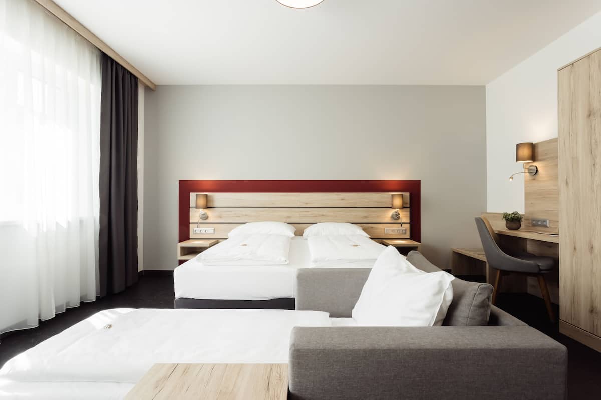 A modern hotel room with a large bed, a desk, and a sofa.