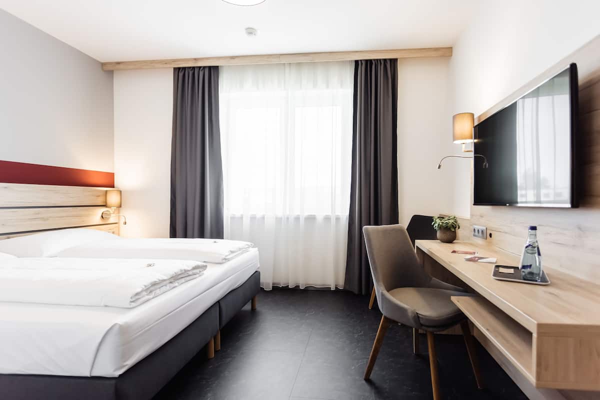 A hotel room with a bed, a desk, a chair, a TV, and a window with curtains.