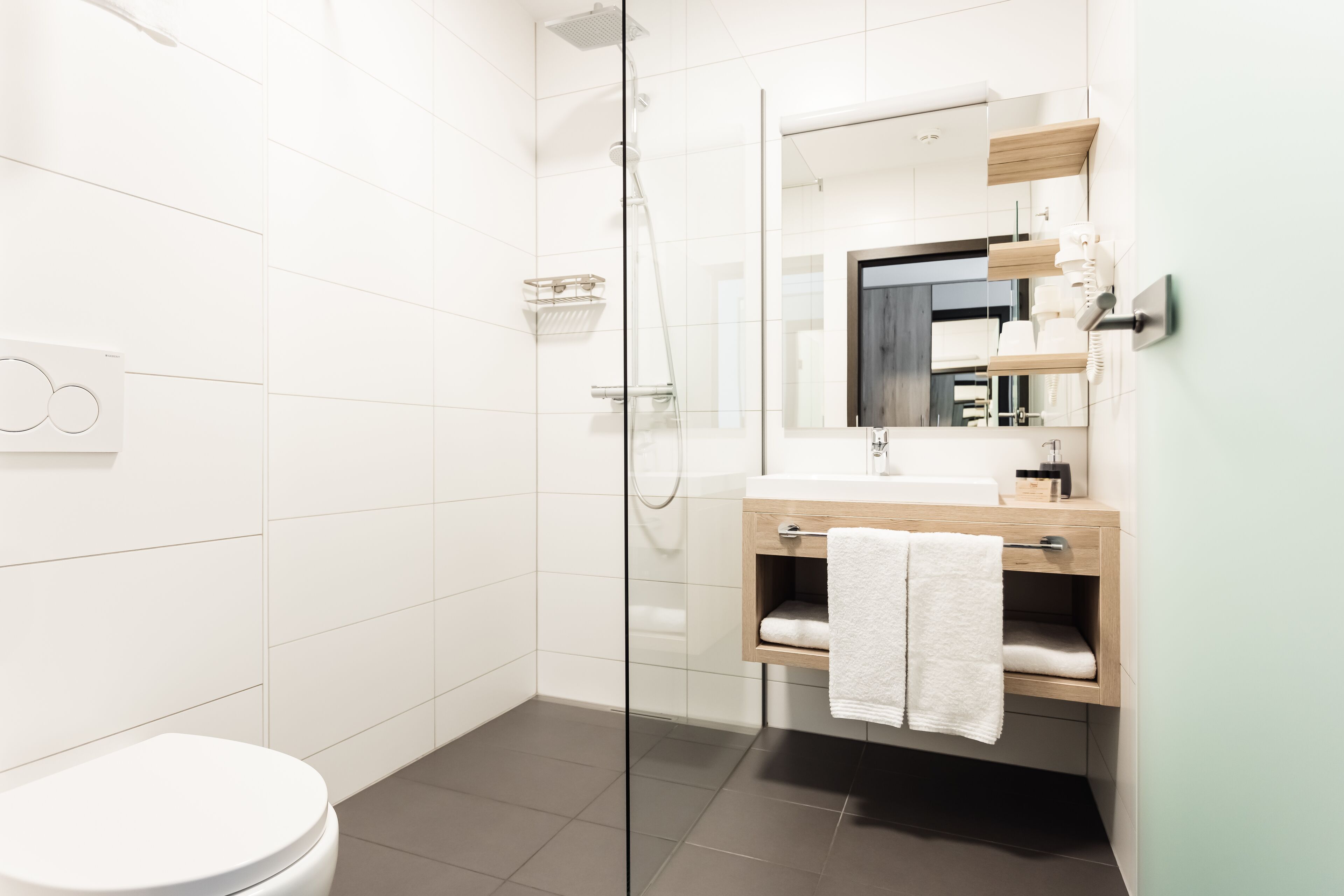 Un baño moderno con ducha de vidrio, inodoro blanco y tocador de madera con espejo.
