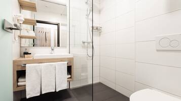 Un baño moderno con cabina de ducha de vidrio, tocador de madera, lavamanos blanco y un inodoro.
