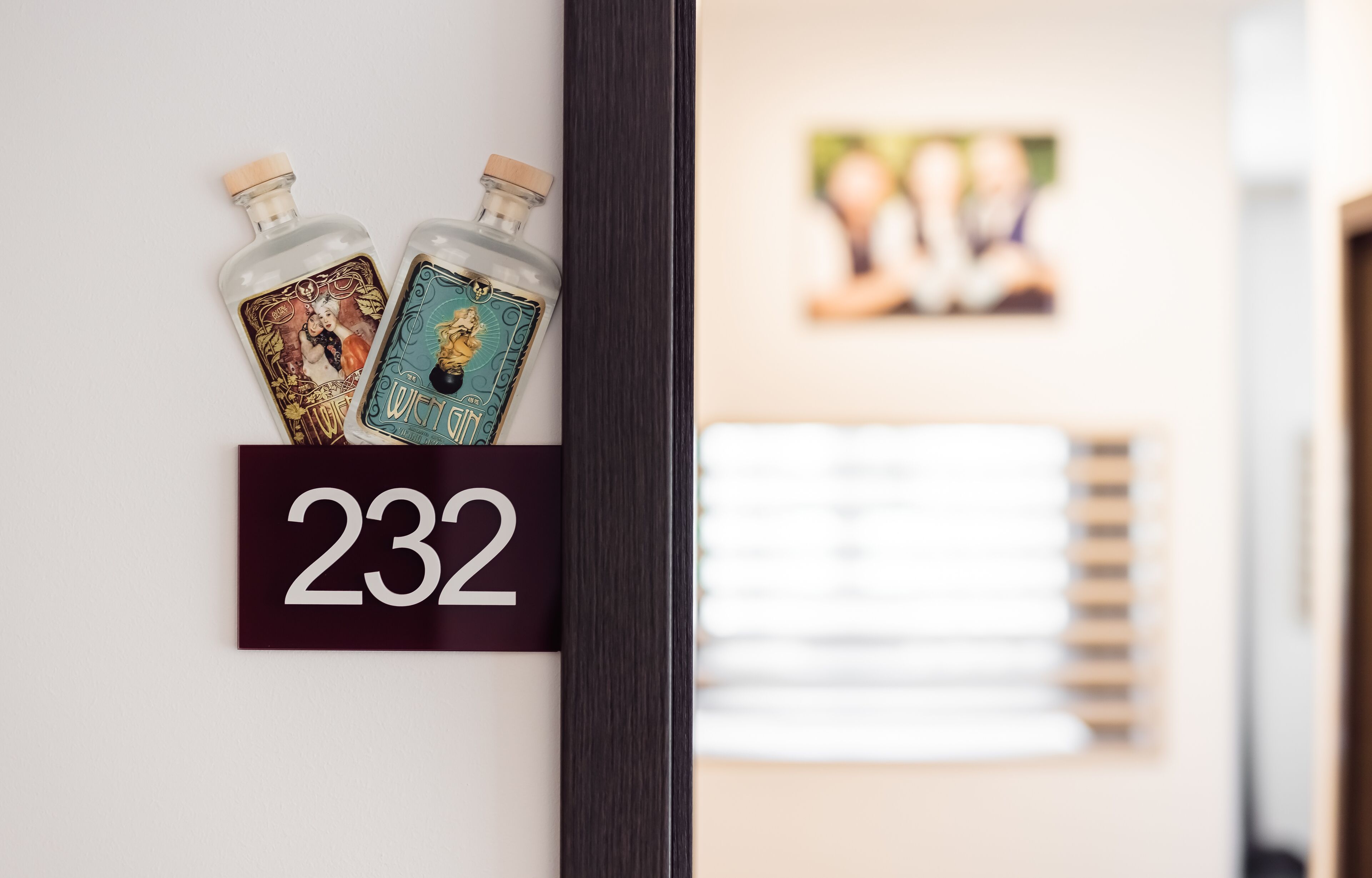 A hotel room number 232 with two bottles of liquor and a framed photo on the wall.