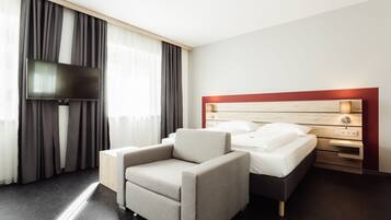 A modern hotel room with a bed, a TV, a sofa, and a bedside table.