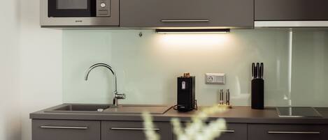 A modern kitchen with a built-in microwave, a sink, and a countertop with a coffee machine and utensils.