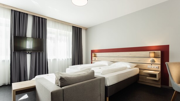 A modern hotel room with a bed, a TV, a desk, and a chair. - Hotel Smart Liv’In (Boheimkirchen)