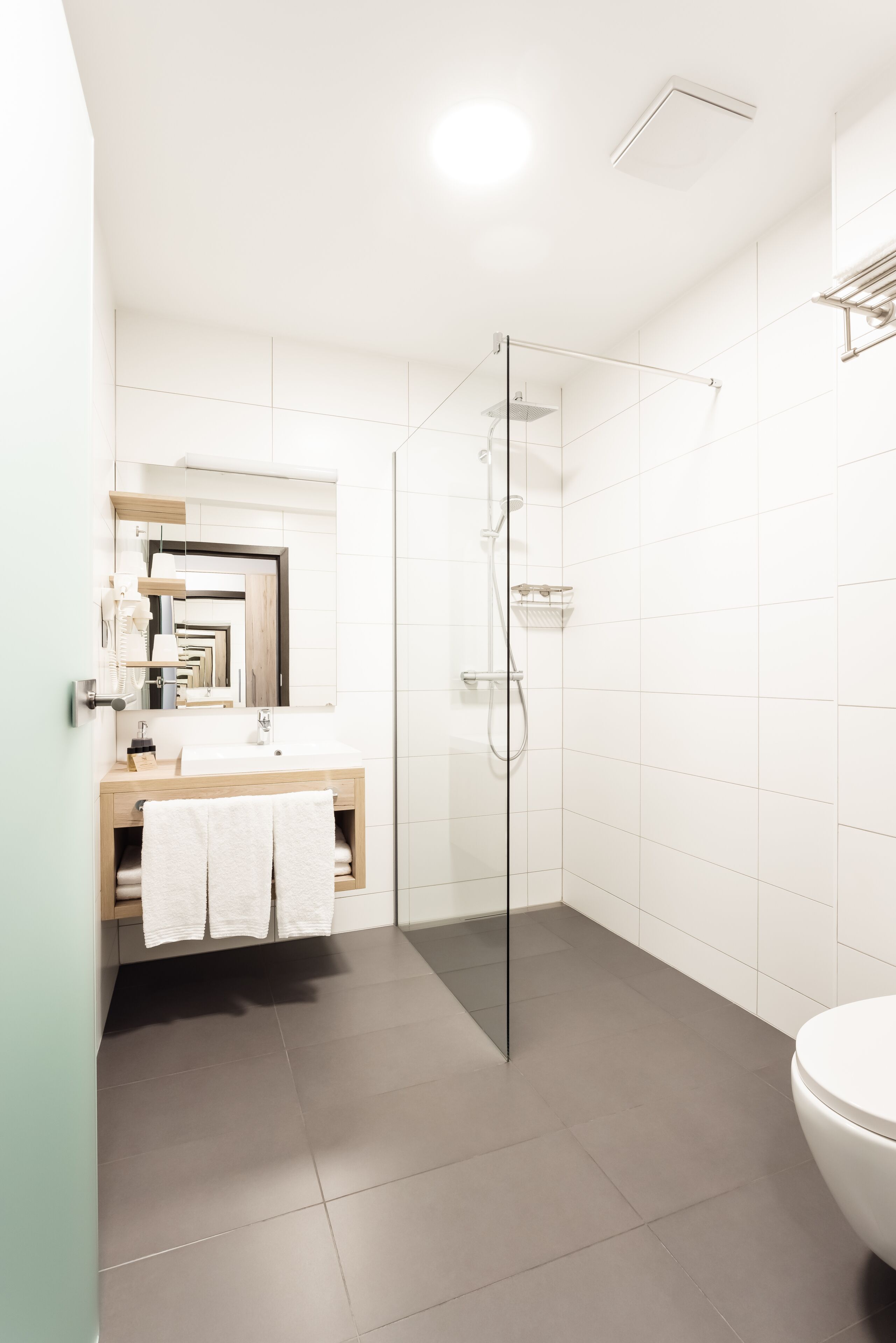 Un bagno moderno con doccia vetro, lavabo e specchio, e un WC.