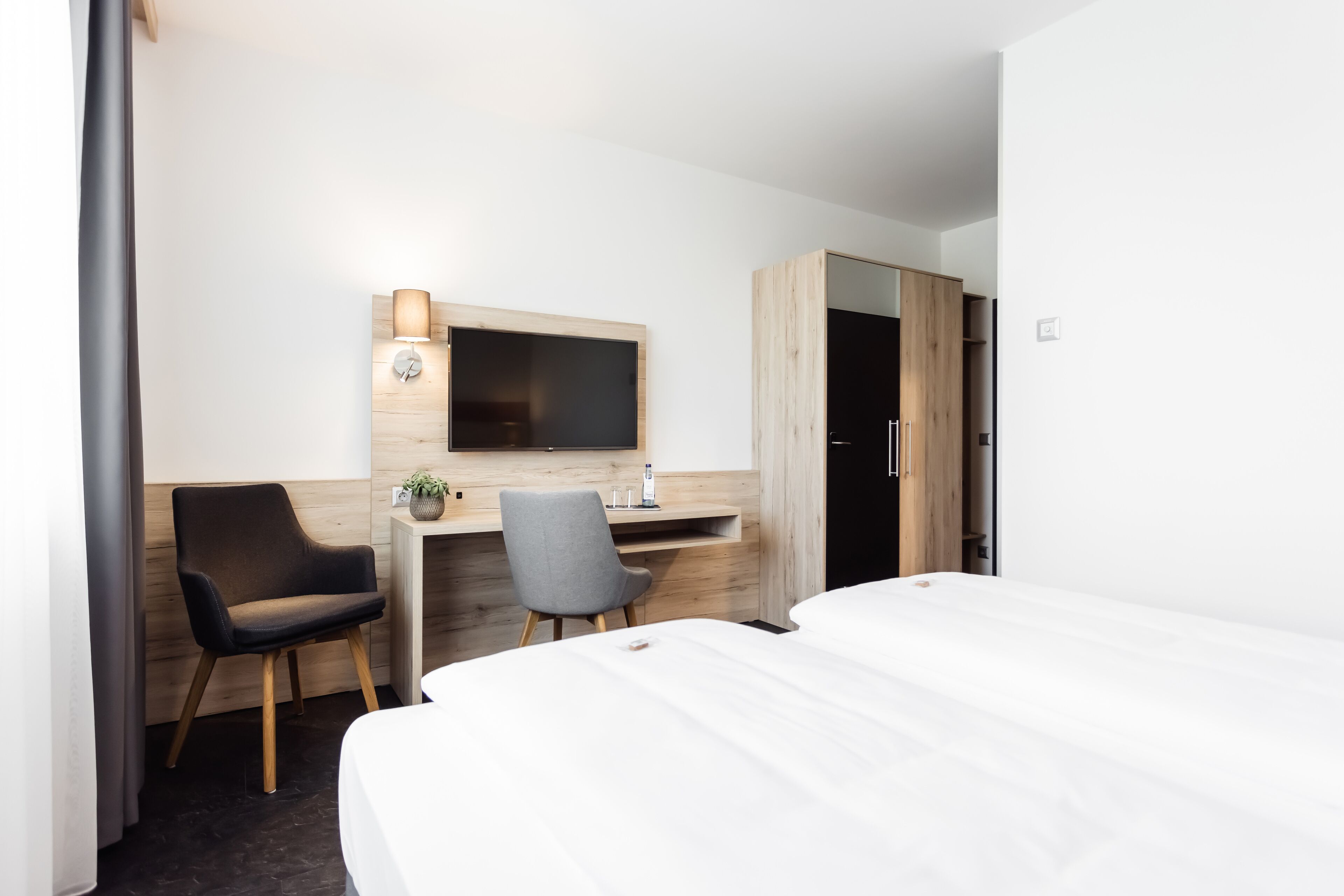 A hotel room with a bed, a desk with a chair, a TV, and a wardrobe.