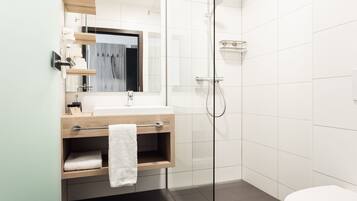 A modern bathroom with a glass-enclosed shower, a wooden vanity with a towel rack, and a white toilet.
