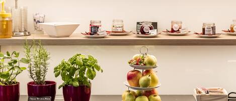 A kitchen counter with various food items, including jars of preserves, bottles of wine, and a fruit display.