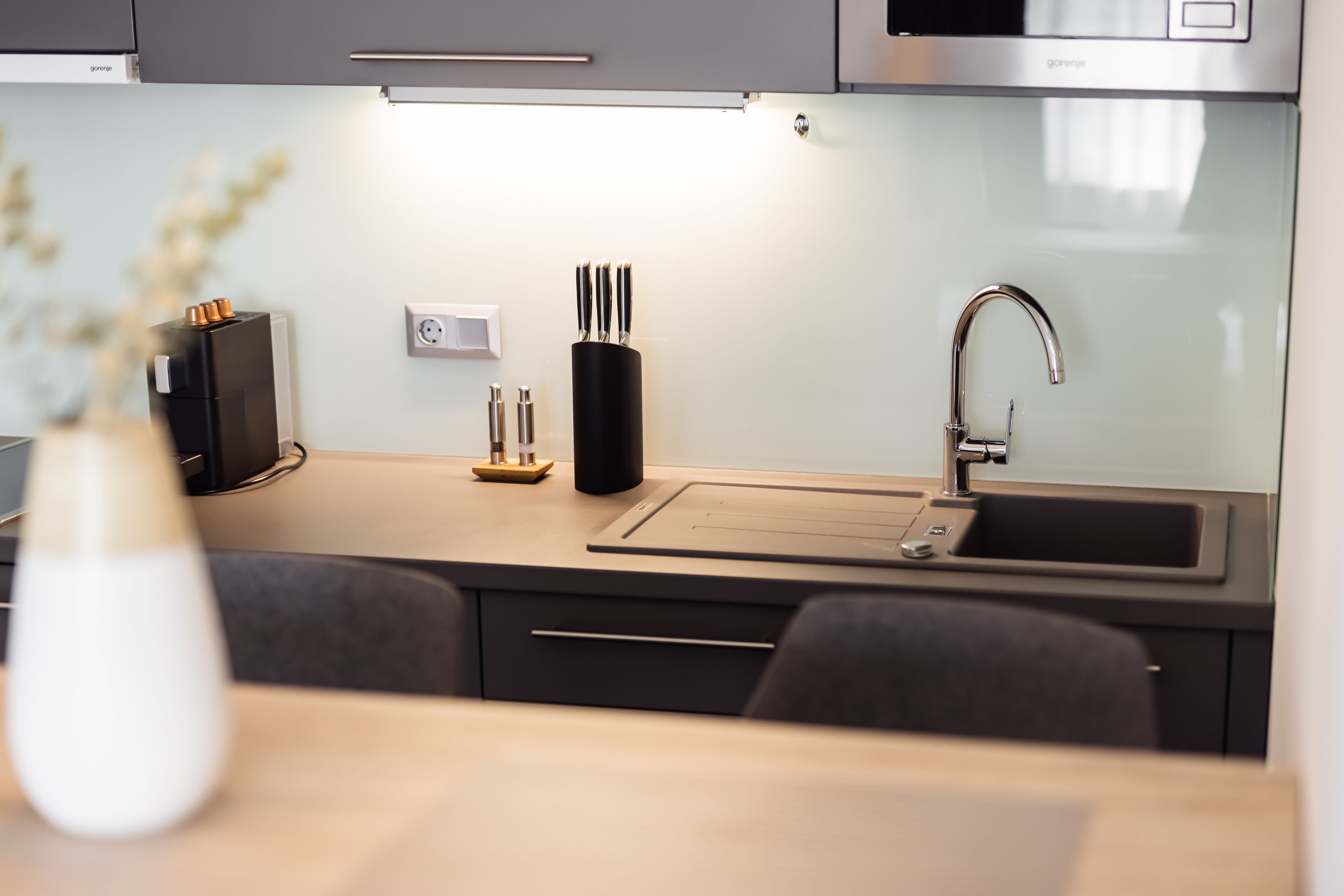 A modern kitchen with a stainless steel sink, a black knife block, and a vase with flowers on the counter.