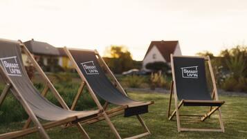 Three wooden lounge chairs with 'Smart Livin' branding, arranged on a grassy lawn with a house and trees in the background.