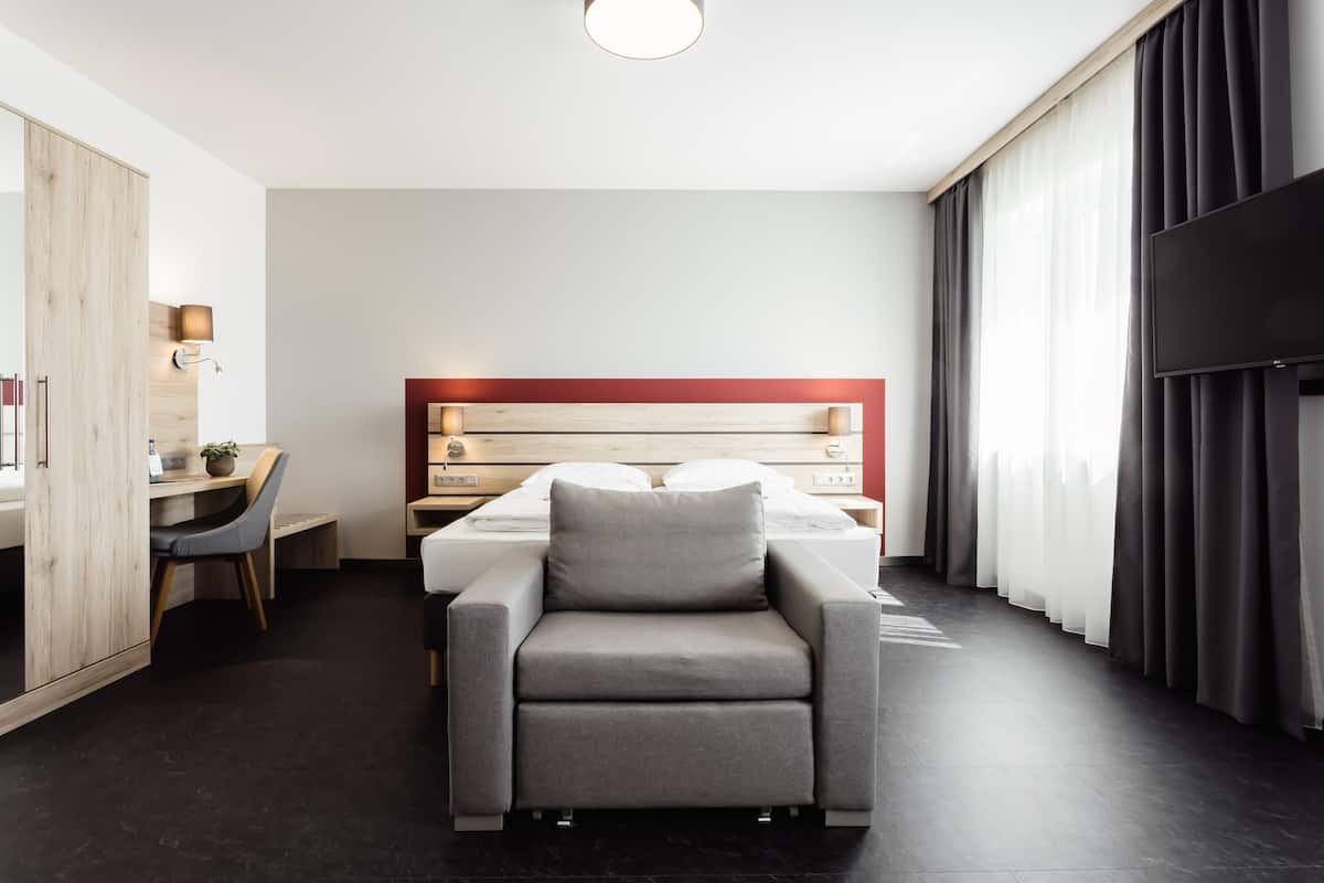 A modern hotel room with a bed, a desk, a chair, and a TV.